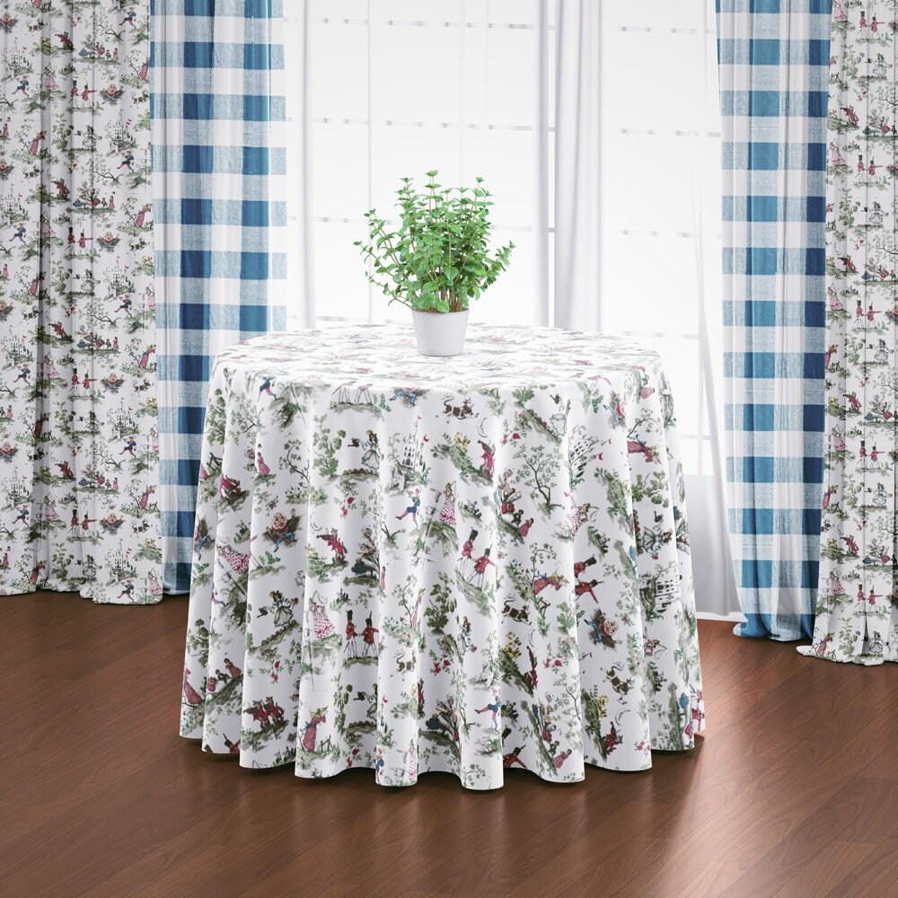 a round table with a white tablecloth adorned with a floral pattern, and a potted plant placed on top of the table. The table is set against a backdrop of blue and white checkered curtains, creating a cozy and inviting atmosphere.
