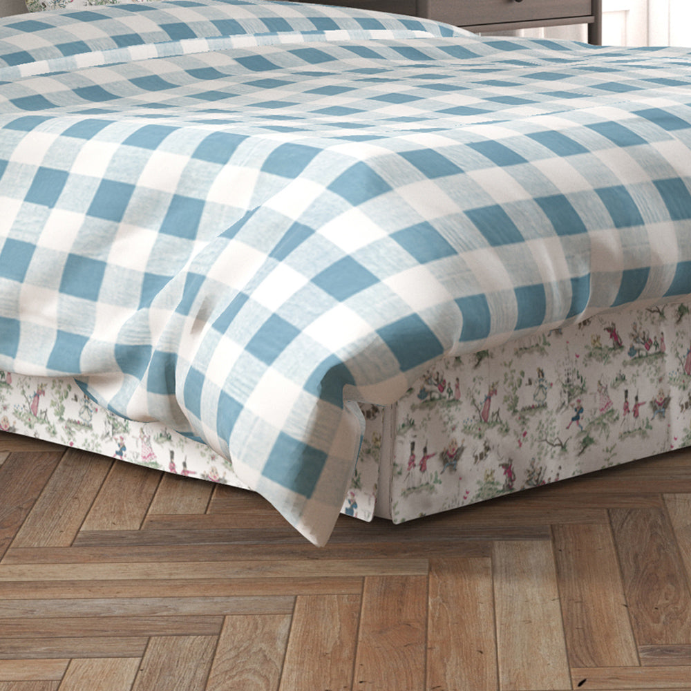 a bed with a blue and white checkered comforter and a floral patterned bed skirt. The bed is placed on a wooden floor.